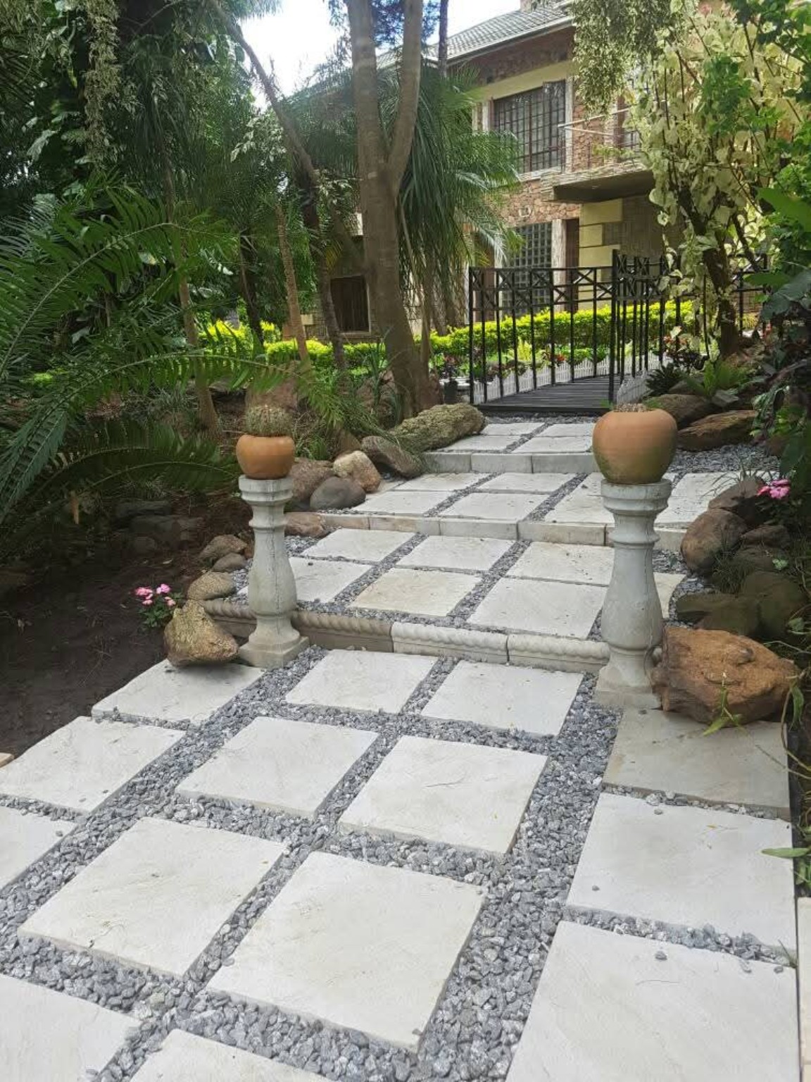 Allée en dalles claires et gravillons au milieu d’un jardin arboré